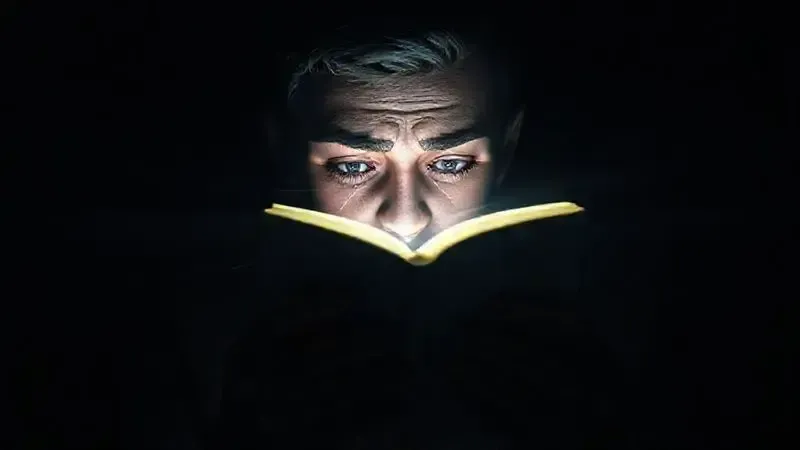 Cena conceitual mostrando leitura com livro iluminado no escuro causando tensão ocular visualizada artisticamente